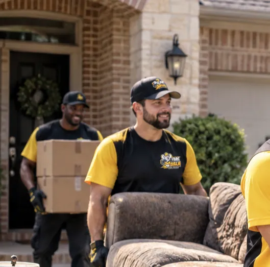 Junk Koala Fort Worth crew carrying a sofa and moving boxes out of the front door of a brick Fort Worth home