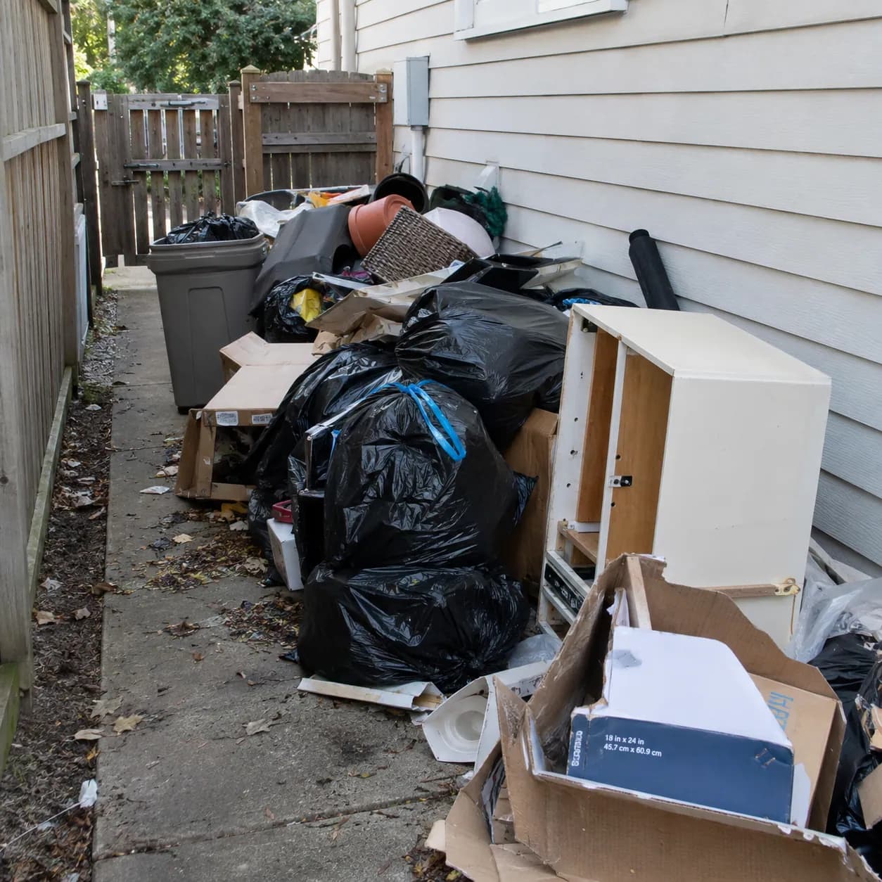 Household junk, bagged trash and broken furniture stacked along the side of a house