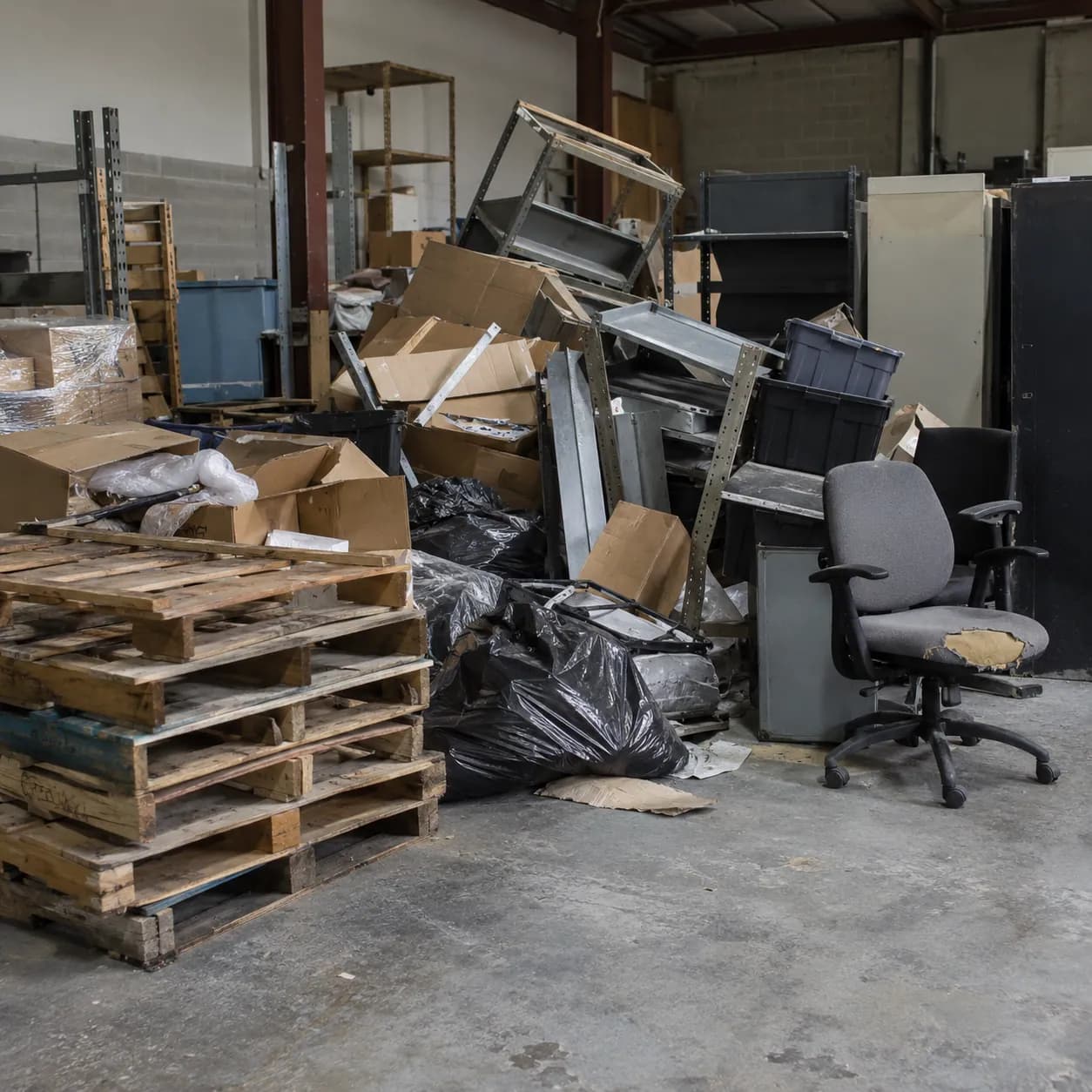Pallets, racking, chairs and packaging waste piled inside a warehouse space